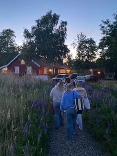 group of people walking in front of a red house at dusk with cars parked nearby