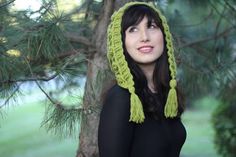 a woman wearing a green knitted hat with tassels in front of a tree