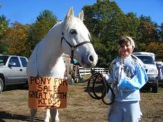 a woman standing next to a white horse with a sign on it's head