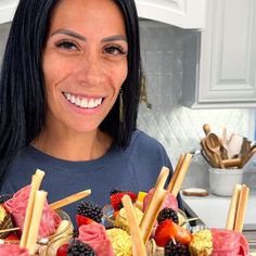 a woman is smiling while holding a platter of fruit and vegtables