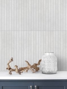 a white vase sitting on top of a counter next to some driftwood pieces in front of a wall