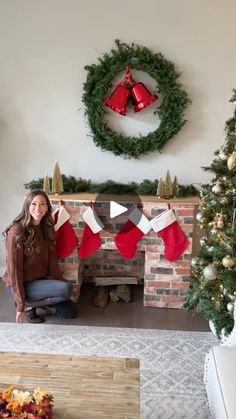 a woman sitting in front of a fireplace with stockings hanging from it's mantle