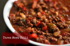 a white bowl filled with chili and meat next to a black sign that says three meat chili