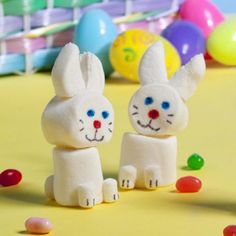 two white bunny figurines sitting next to each other on a table with candy