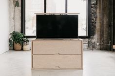 a television sitting on top of a wooden cabinet in an empty room with large windows