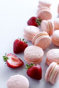 some pink macaroons and strawberries on a white surface with drops of water