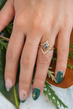 a woman's hand with green and gold nail polish holding a ring on her finger