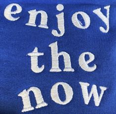 the words enjoy the now written in white on a blue sweater