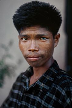 a man with black hair and blue eyes looking at the camera