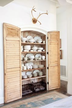 an open cabinet with dishes in it and antlers hanging from the wall above them