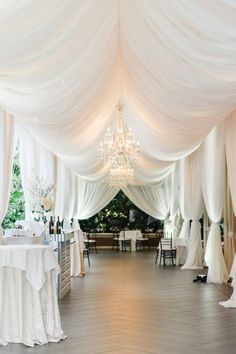 the inside of a wedding reception with white drapes and chandelier