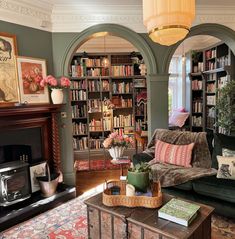 a living room filled with furniture and bookshelves next to a fire place under a chandelier