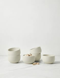 three white bowls with gold coins in them on a marble countertop next to each other