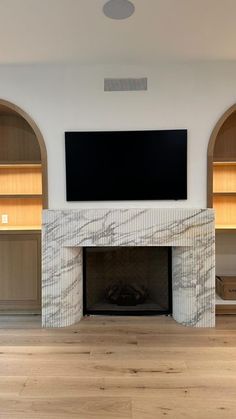 an empty living room with a tv mounted above the fireplace and built - in bookshelves