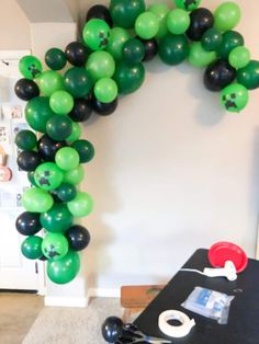 green and black balloons are arranged in the shape of a wreath on a wall above a table