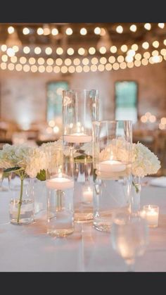 white flowers and candles are arranged on a table in front of the chandelier