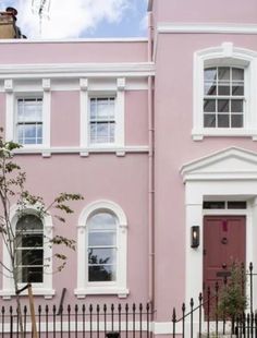 a pink house with white trim on the front door and windows, next to a black fence