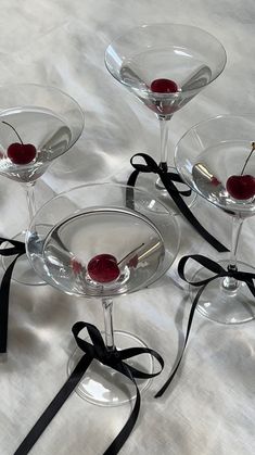 four martini glasses with cherries in them on a white tablecloth, tied with black ribbon