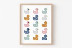 an art print with rubber ducks in pastel colors on a white wall next to a wooden frame