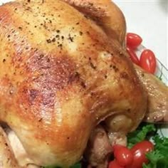 a whole chicken sitting on top of a white plate with tomatoes and lettuce