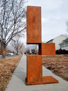 a metal sculpture sitting on the side of a sidewalk next to a tree and houses