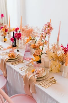 the table is set with pink chairs and white linens, goldware, candles, and flowers