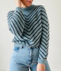 a woman wearing a sweater and jeans is talking on her cell phone while standing in front of a white wall