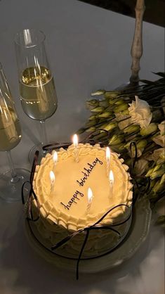 a birthday cake sitting on top of a table next to some wine glasses and flowers