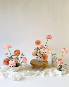 several vases with flowers in them on a white table cloth next to a candle holder