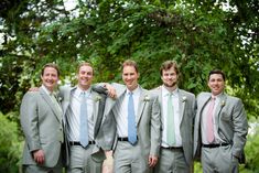 a group of men standing next to each other wearing suits and ties with trees in the background