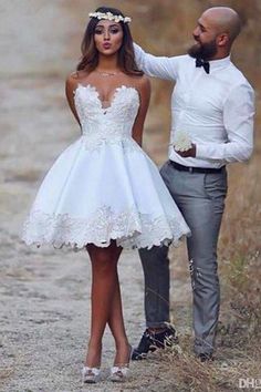 a man standing next to a woman in a white dress on a dirt road with grass