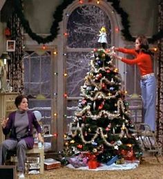 two women decorating a christmas tree in a living room