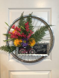 a bicycle wheel hanging on the wall with flowers in it and a sign that says enjoy the journey