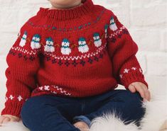 a young child wearing a red sweater with snowmen on it, sitting in front of a white brick wall