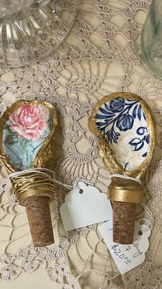 two wine corks with tags attached to them sitting on a lace tablecloth covered table