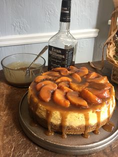 a cheesecake with caramel topping on a plate next to a bottle of booze