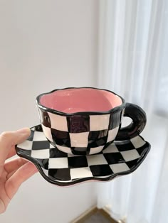 a hand holding a black and white checkered coffee cup with saucer on it