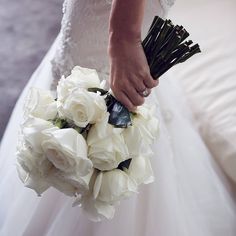 a woman in a wedding dress holding a bouquet of white roses and greenery with her hand