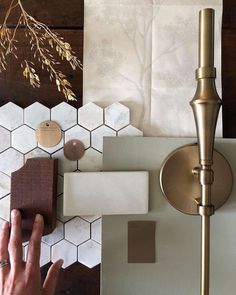 a person's hand is on the wall next to some tiles and a gold faucet