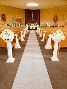 the aisle is lined with white flowers and pews