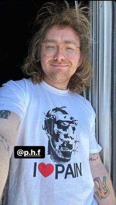 a man with long hair and glasses wearing a shirt that says i love pain on it