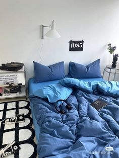 an unmade bed with blue sheets and pillows in a white room next to a black and white rug