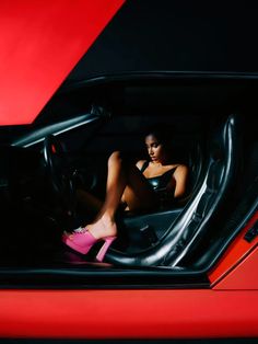 a woman sitting in the driver's seat of a red sports car with her feet up