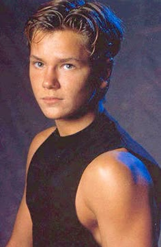 the young man is posing for a photo in his black shirt and vest, with blue eyes