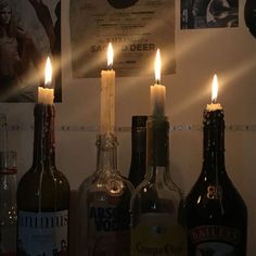 three bottles with candles in them sitting on a shelf next to some posters and pictures