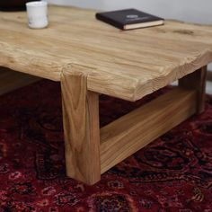 a wooden table sitting on top of a red rug next to a book and cup