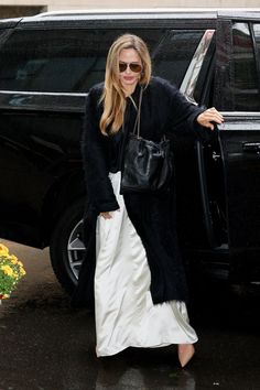 a woman in black and white is walking out of a car with her hand on the door