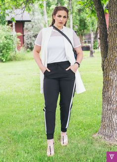 a woman standing in front of a tree wearing black pants and a white top with sheer sleeves