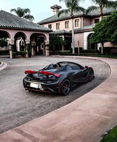 a black and red sports car parked in front of a large house with palm trees