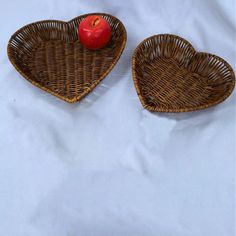 two wicker heart shaped baskets with an apple in the middle on a white sheet